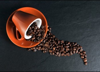 coffee beans spilling out of an orange coffee cup on an orange saucer