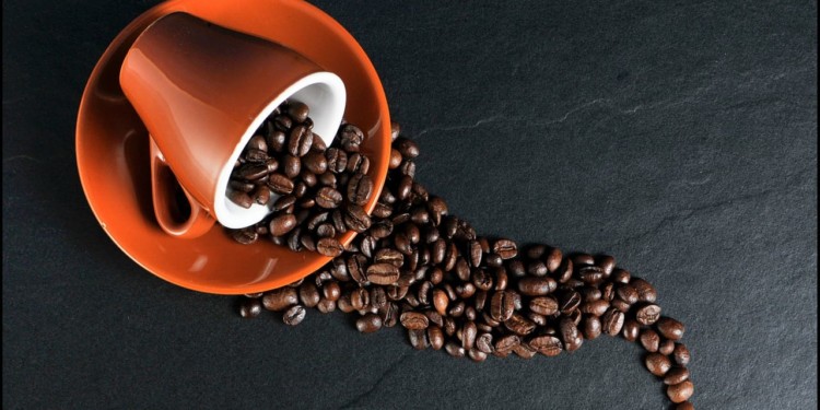 coffee beans spilling out of an orange coffee cup on an orange saucer