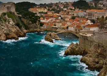 Orange roofed homes and blue ocean crashing against the rocky shores in the coast of Croatia