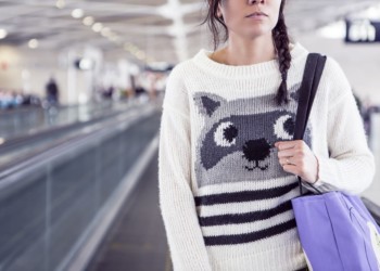 woman wearing a raccoon sweater on moving walkway in airport