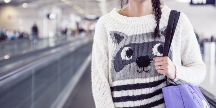 woman wearing a raccoon sweater on moving walkway in airport