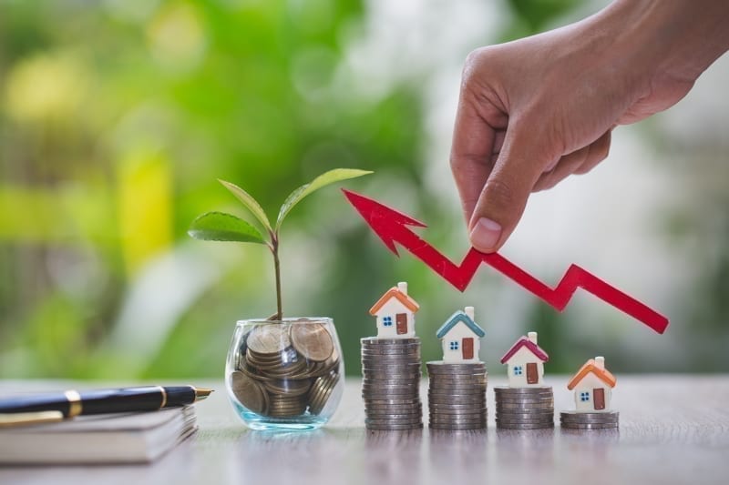 Businessperson's Hand Holding Arrow Over Stacked Coins With House Models. Real estate investment concept.