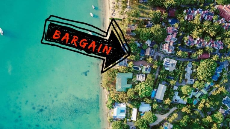 An aerial view down at homes along the beach with an arrow pointing to bargain properties. Buying cheap real estate overseas