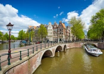 Beautiful Amsterdam Canal with buildings in the background and a boat on the water.