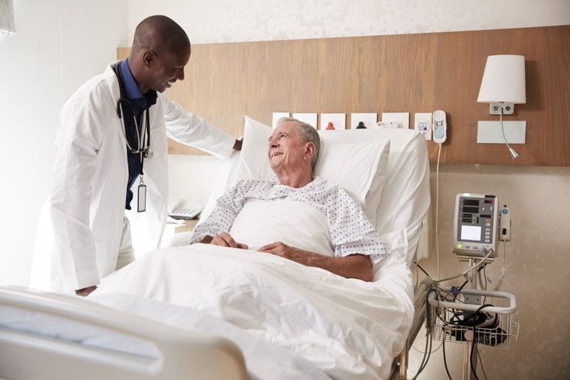 Doctor Visiting And Talking With Senior Male Patient In Hospital Bed. health care in belize