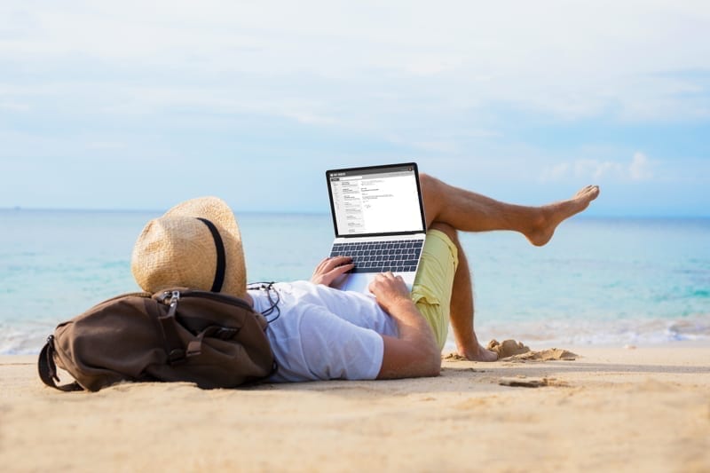 Male writing on laptop while relaxing on beach