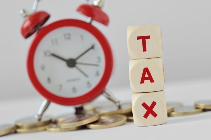 The word Tax written with wooden blocks and alarm clock on coins in the background.