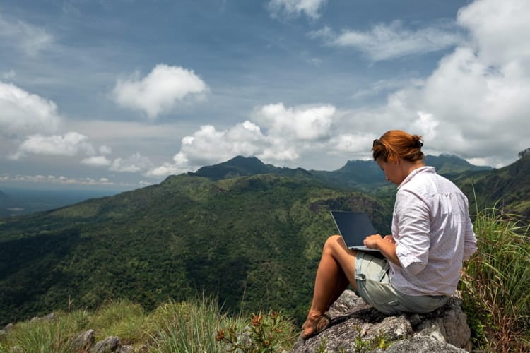 Girl working on her computer on the top of the mountain.