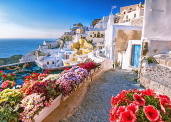 Scenic view of traditional cycladic houses on small street with flowers in foreground, Oia village, Santorini, Greece. how to buy a rental property