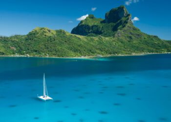 Catamaran sailing boat in the clear blue water lagoon of Bora Bora.