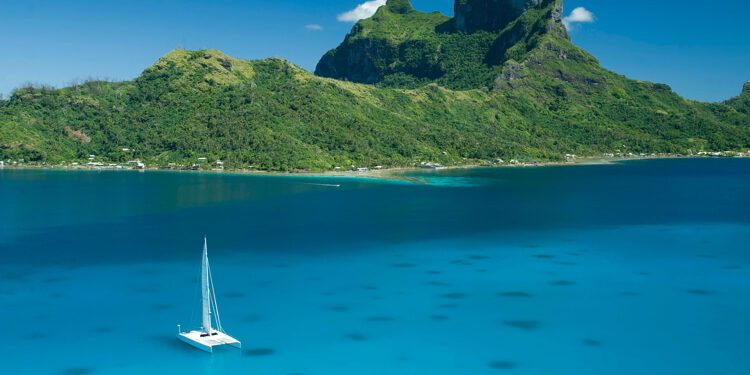 Catamaran sailing boat in the clear blue water lagoon of Bora Bora.