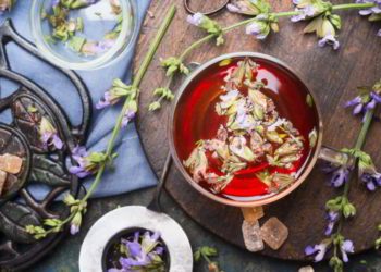 Cup of herbal tea with fresh herbs and aged vintage tea set, top view, close up