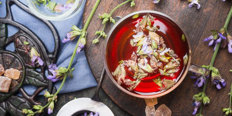 Cup of herbal tea with fresh herbs and aged vintage tea set, top view, close up