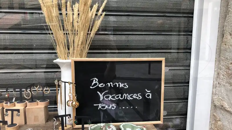 Shop window with a chalkboard sign reading "Bonnes vacances à tous" and handmade jewelry on display.