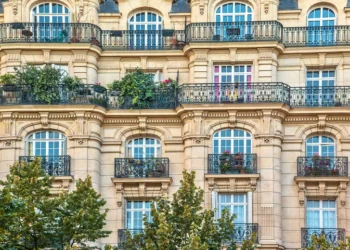 Link: Street view of an old, elegant residential building facade in Paris, with ornate details in the stone walls, french doors and wrought iron railings on the balconies