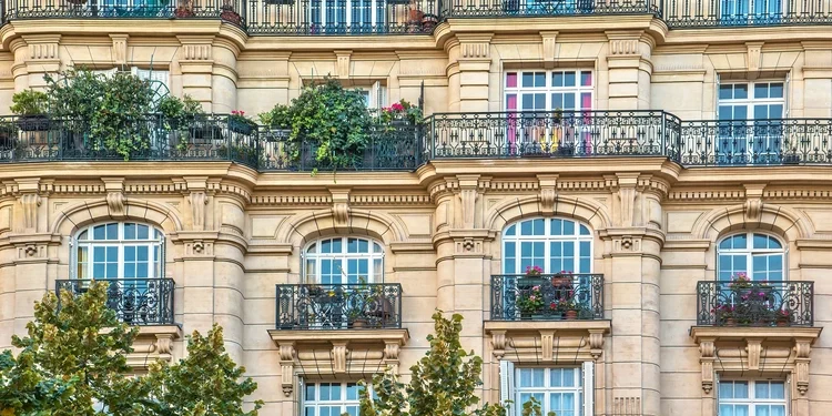 Link: Street view of an old, elegant residential building facade in Paris, with ornate details in the stone walls, french doors and wrought iron railings on the balconies