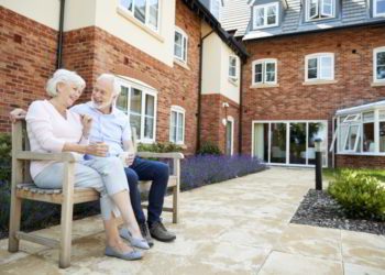 Retired couple sitting on bench with hot drink in assisted living facility