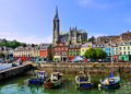 Colorful buildings and old boats with cathedral in background in the harbor of Cobh, County Cork, Ireland Living In Ireland