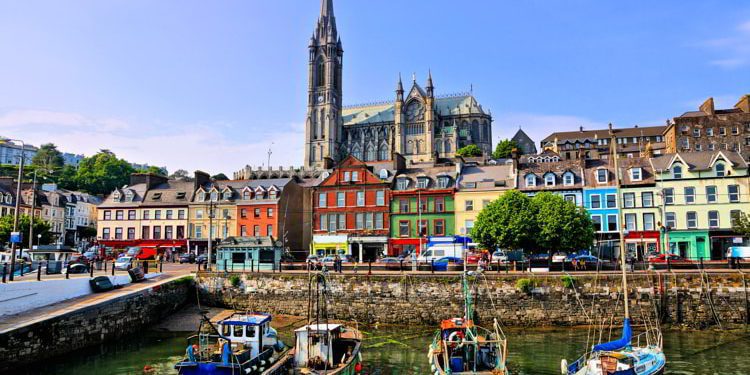 Colorful buildings and old boats with cathedral in background in the harbor of Cobh, County Cork, Ireland Living In Ireland