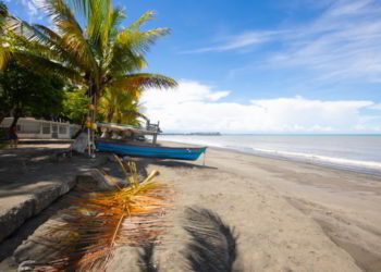 A white sand beach in Puerto Armuelles with palm trees and a blue boat