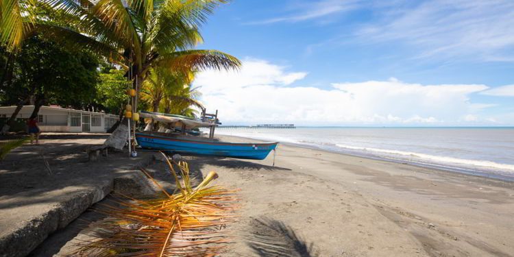 A white sand beach in Puerto Armuelles with palm trees and a blue boat