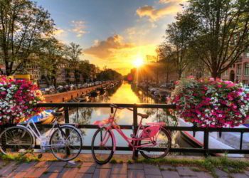 Beautiful sunrise over Amsterdam, The Netherlands, with flowers and bicycles on the bridge in spring