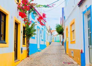 A cobblestone street in the Algarve, Portugal with colorful houses and red flowers