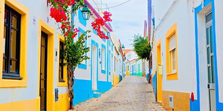 A cobblestone street in the Algarve, Portugal with colorful houses and red flowers