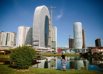 Tourist girl in a hat and with a backpack on the background of modern high-rise buildings in Batumi, Adjara, Georgia.