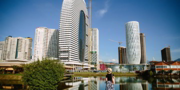 Tourist girl in a hat and with a backpack on the background of modern high-rise buildings in Batumi, Adjara, Georgia.