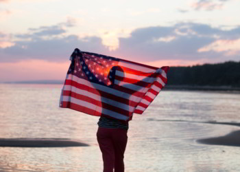 A woman with an American flag at the beach at sunset