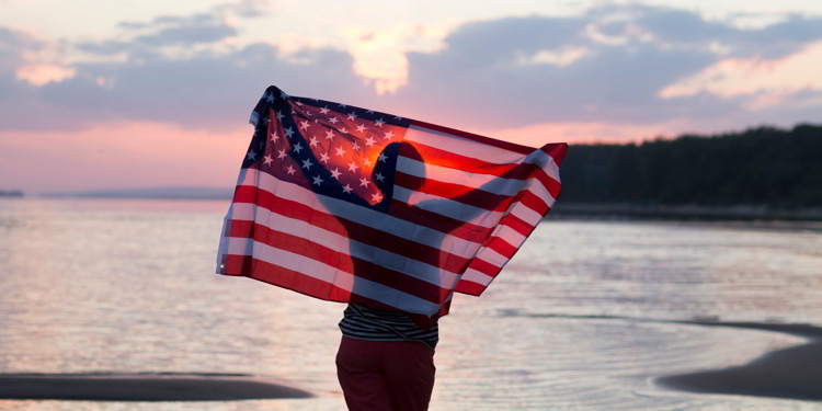 A woman with an American flag at the beach at sunset