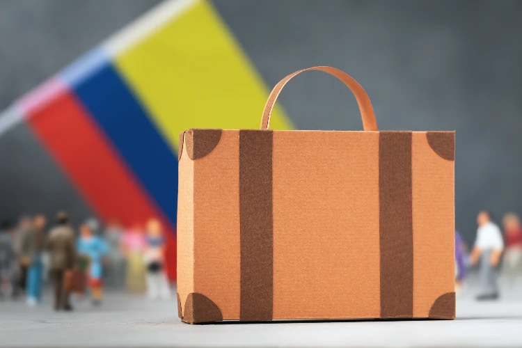 Cardboard suitcase, plastic toy people and the Colombian flag on an abstract background
