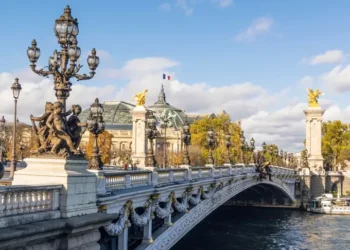 Pont Alexandre III bridge on sunny autumn day. Behind is roof of Grand Palais with French flag waiving against clouds