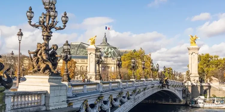 Pont Alexandre III bridge on sunny autumn day. Behind is roof of Grand Palais with French flag waiving against clouds