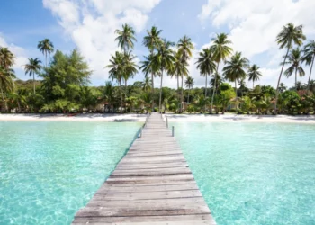 Beach with turquoise water, wooden pier and tropical palm trees, in Thailand,