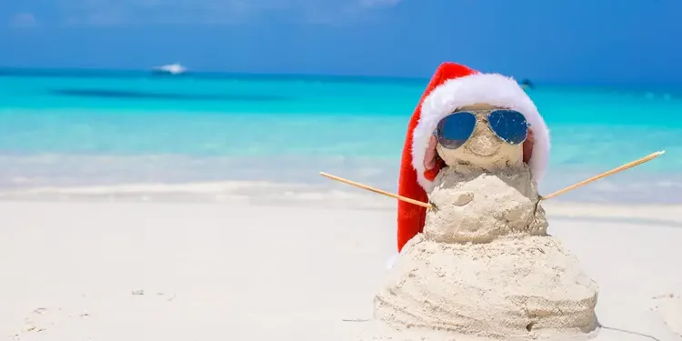 Sandy snowman with red Santa Hat on white Caribbean beach. Legend Among Travelers