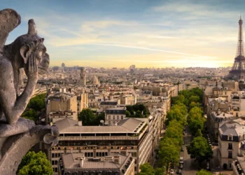 A rock gargoyle sits atop of a building in Paris, France