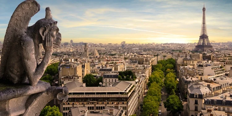 A rock gargoyle sits atop of a building in Paris, France