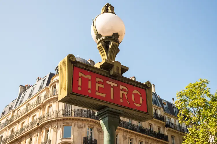 A traditional Paris Metro sign with buildings in the background. Europe Cities