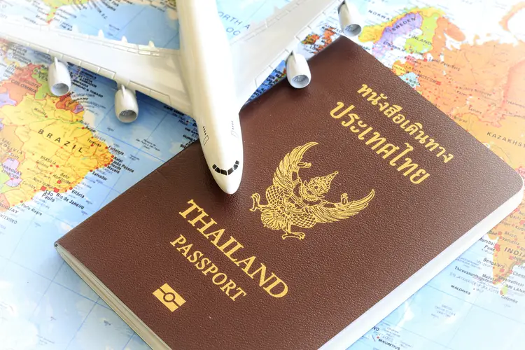 Toy plane resting on a thailand passport and world map. retire in thailand