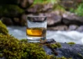 Glass of strong scotch single malt whisky with fast flowing mountain river on background. liquid gold