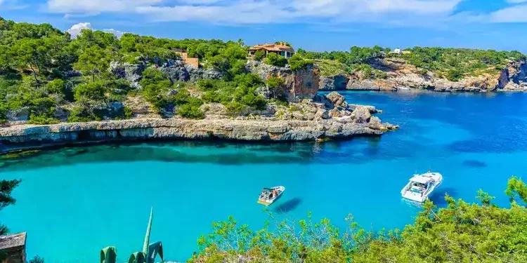 Summer vacation scene with sailboats on turquoise clean water on Mallorca Island near Cala Llombards beach.