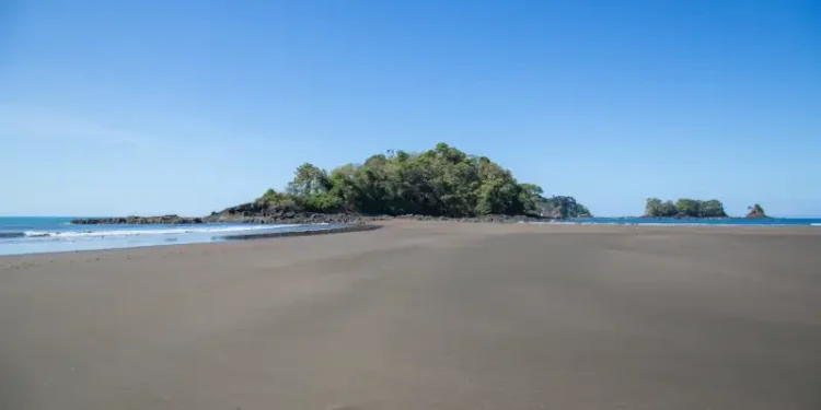 tidal island connected to the mainland by a wide, flat area of sand, likely exposed during low tide