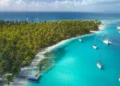 Drone Aerial View of Sailboats & Sailing Yachts anchored in turquoise Water of Blue Lagoon next to white Sand Beach of Tropical Caribbean Island with green Palm Trees.