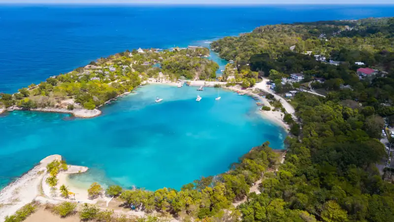 Aerial view of a lush coastline with turquoise water and boats in a calm bay.