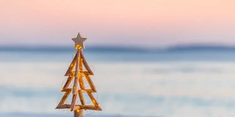 Christmas tree with fairy lights on the beach in summer