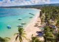 Aerial drone panoramic view of the paradise beach with sandy shore, coral spots, palm trees, color boats and blue water of Atlantic Ocean, Las Terrenas, Samana, Dominican Republic