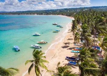 Aerial drone panoramic view of the paradise beach with sandy shore, coral spots, palm trees, color boats and blue water of Atlantic Ocean, Las Terrenas, Samana, Dominican Republic