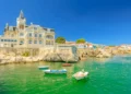 Scenic landscape of abandoned Palace Seixas and boats on the waterfront of Cascais, Lisbon Coast in Portugal. Praia da Rainha on the distance. Turquoise sea in summertime.